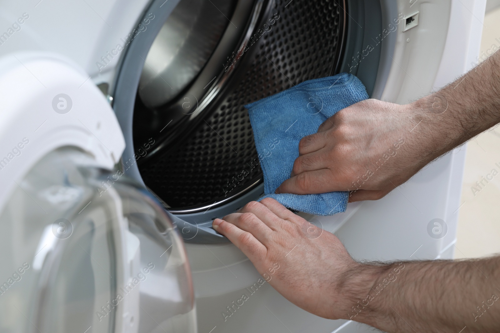 Photo of Man cleaning empty washing machine with rag, closeup