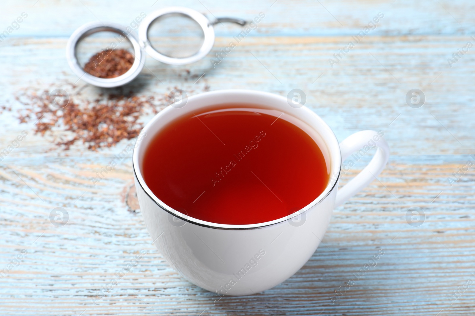 Photo of Freshly brewed rooibos tea and dry leaves on light wooden table