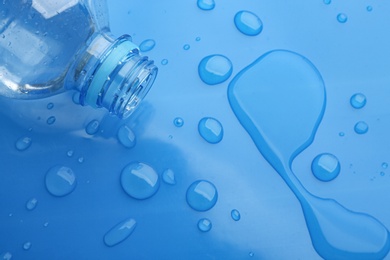 Photo of Drops of spilled water and plastic bottle on blue background, top view