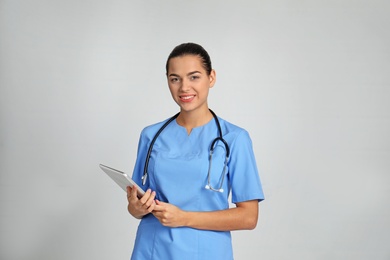 Portrait of young medical assistant with stethoscope and tablet on color background