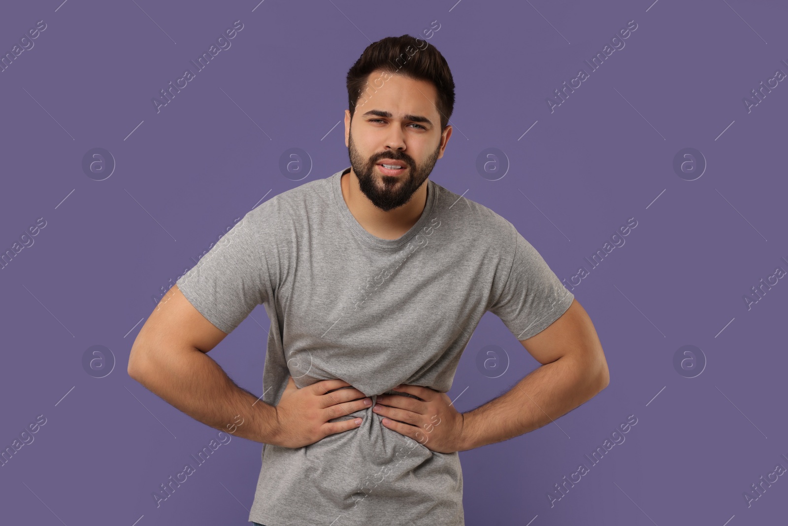 Photo of Young man suffering from stomach pain on purple background