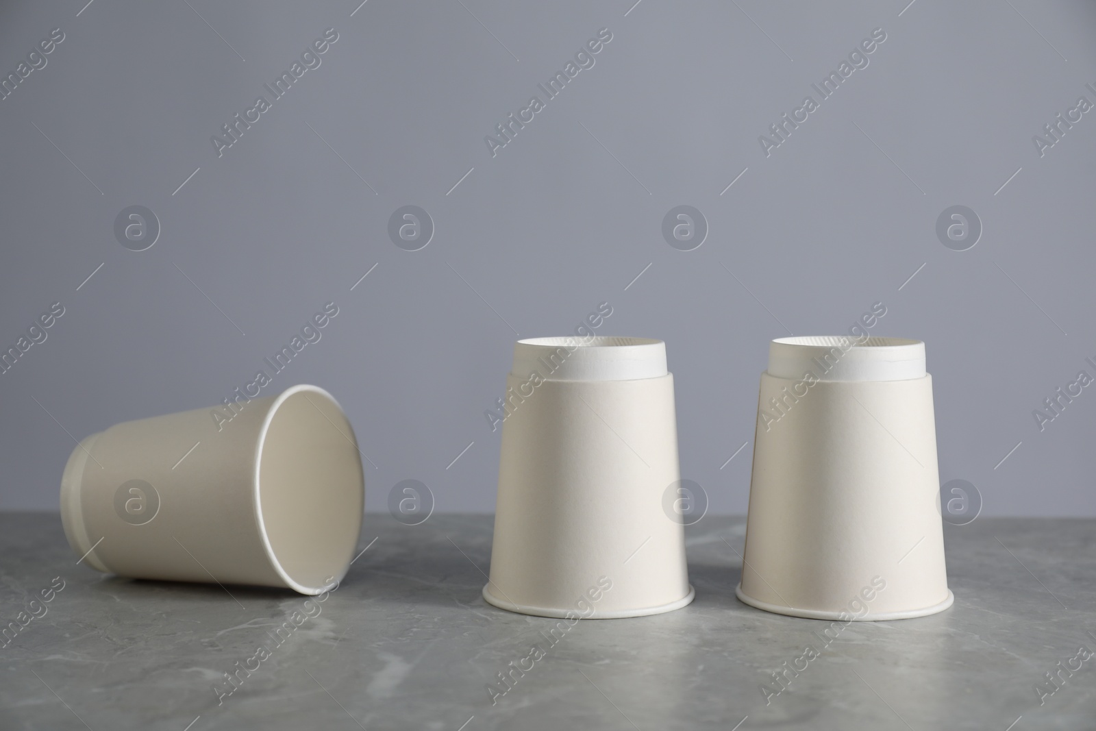 Photo of Shell game. Three paper cups on grey marble table