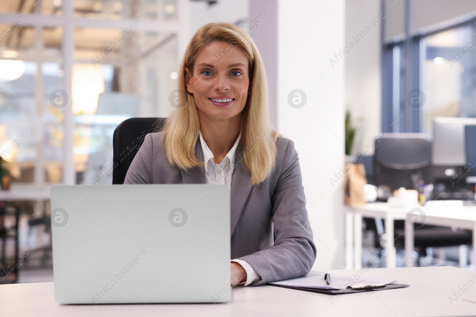 Photo of Smiling woman working with laptop at table in office. Lawyer, businesswoman, accountant or manager