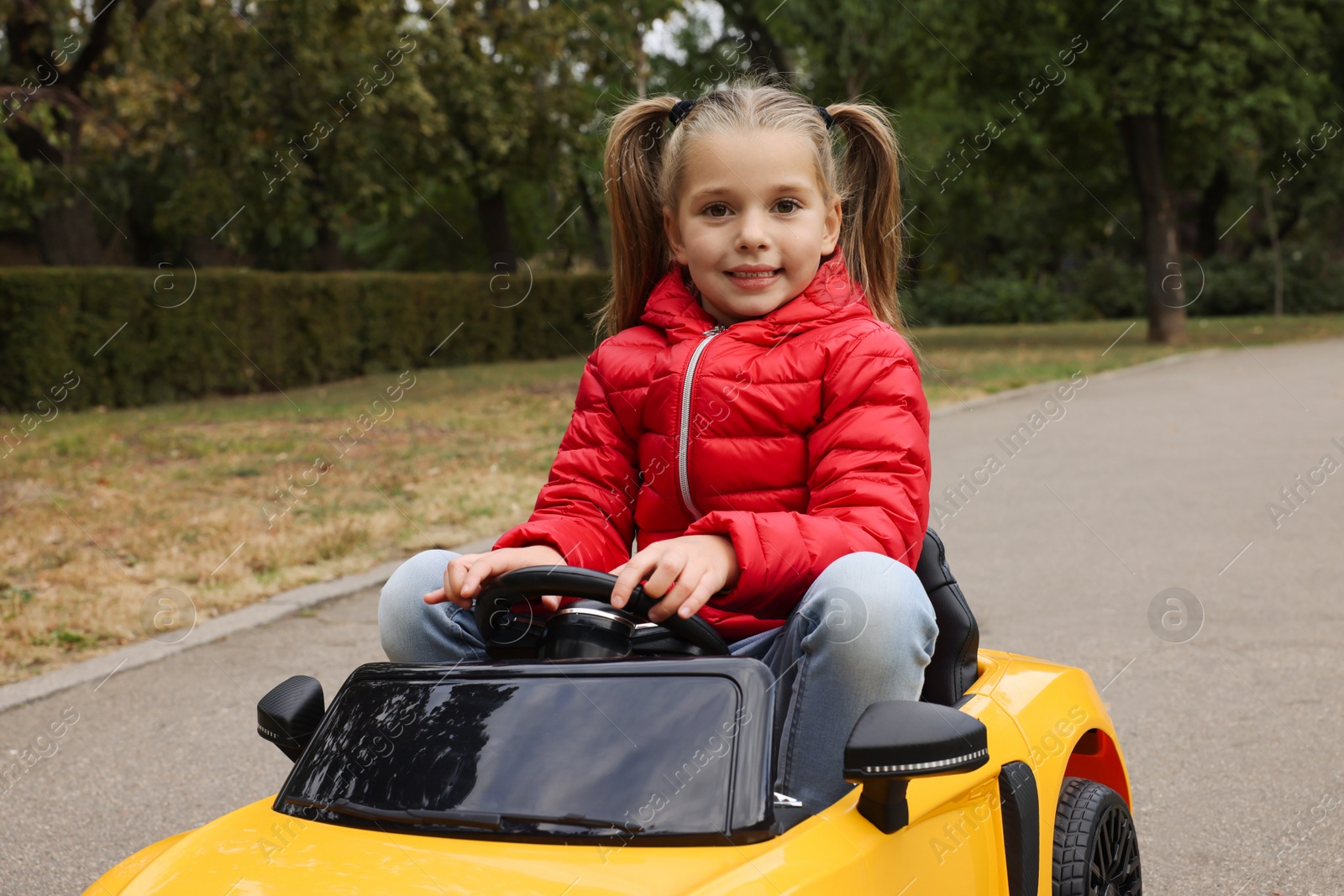 Photo of Cute little girl driving children's car outdoors