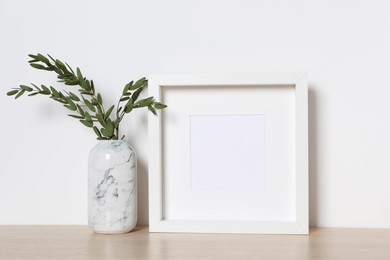 Photo of Empty photo frame and vase with decorative leaves on white table. Mockup for design