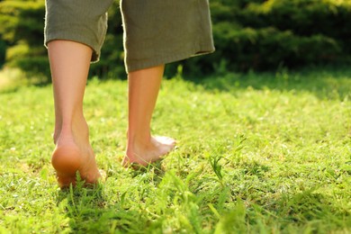Photo of Woman walking barefoot on green grass outdoors, closeup. Space for text