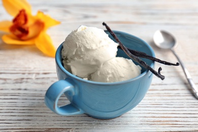 Photo of Cup with tasty vanilla ice cream on wooden background