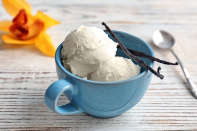 Cup with tasty vanilla ice cream on wooden background