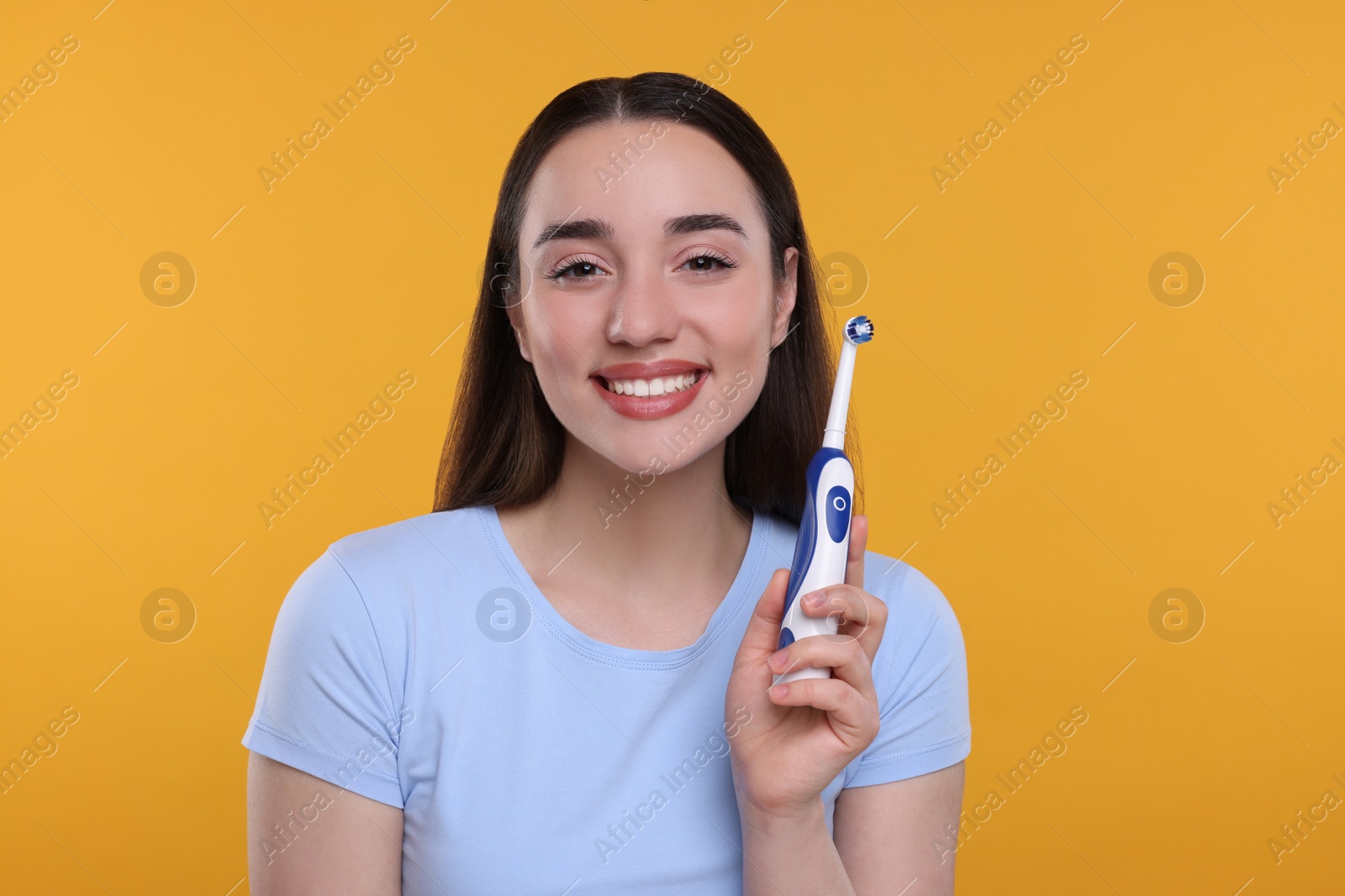 Photo of Happy young woman holding electric toothbrush on yellow background