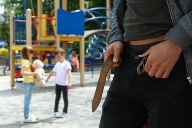 Suspicious adult man taking off his pants at playground with little kids, space for text. Child in danger
