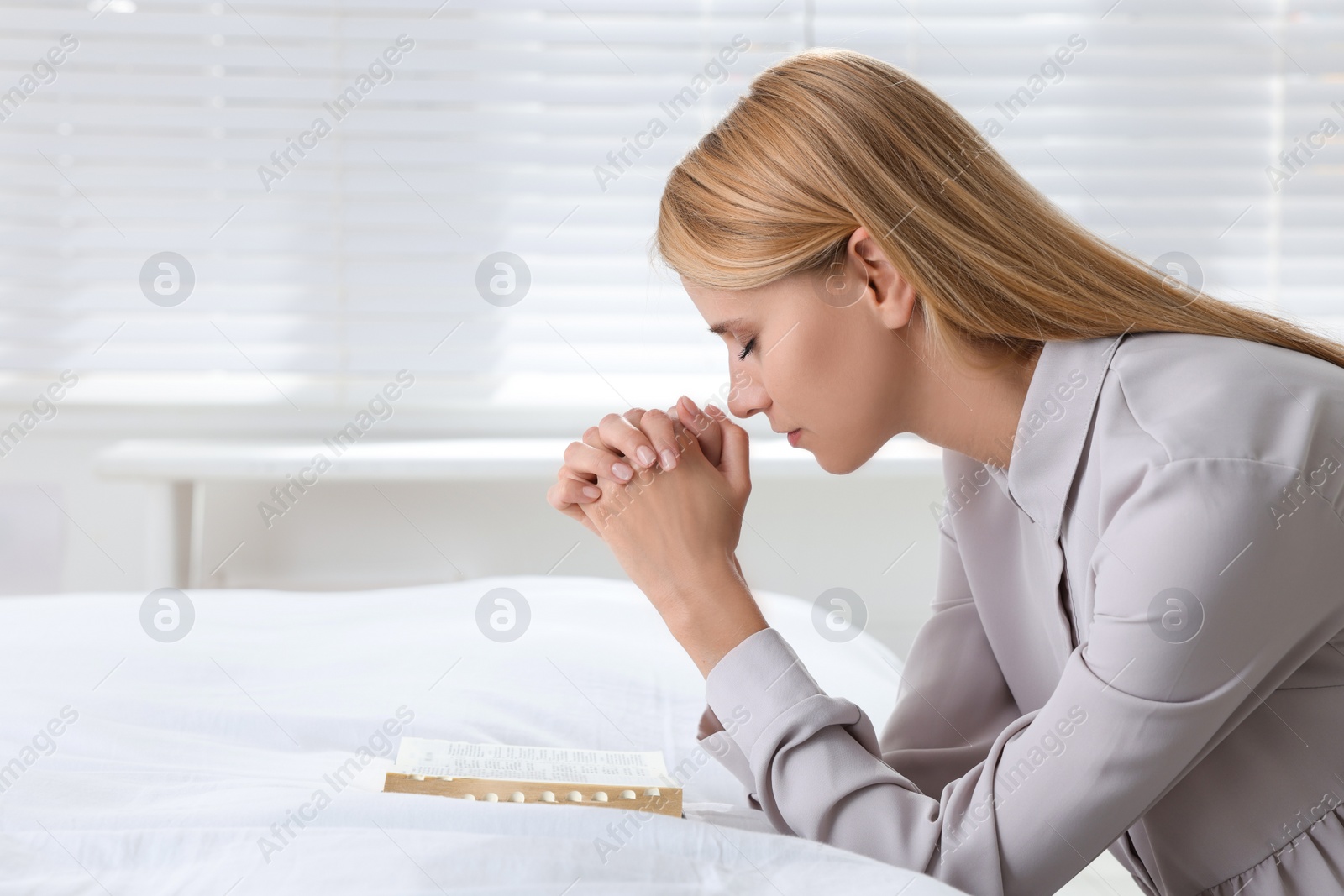 Photo of Religious young woman with Bible praying in bedroom. Space for text