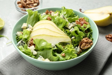 Tasty salad with pear slices, lettuce and walnuts on table, closeup