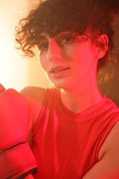 Beautiful young woman with boxing gloves on color background in neon lights and smoke, closeup