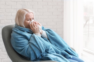 Mature woman wrapped in blanket suffering from cold at home