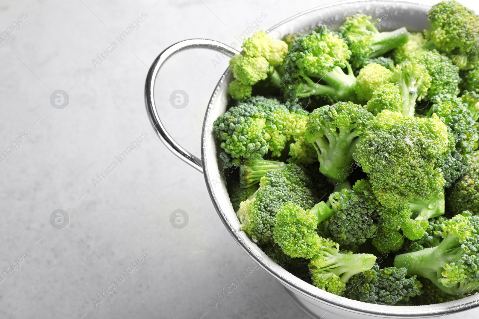 Photo of Colander with fresh green broccoli on grey background