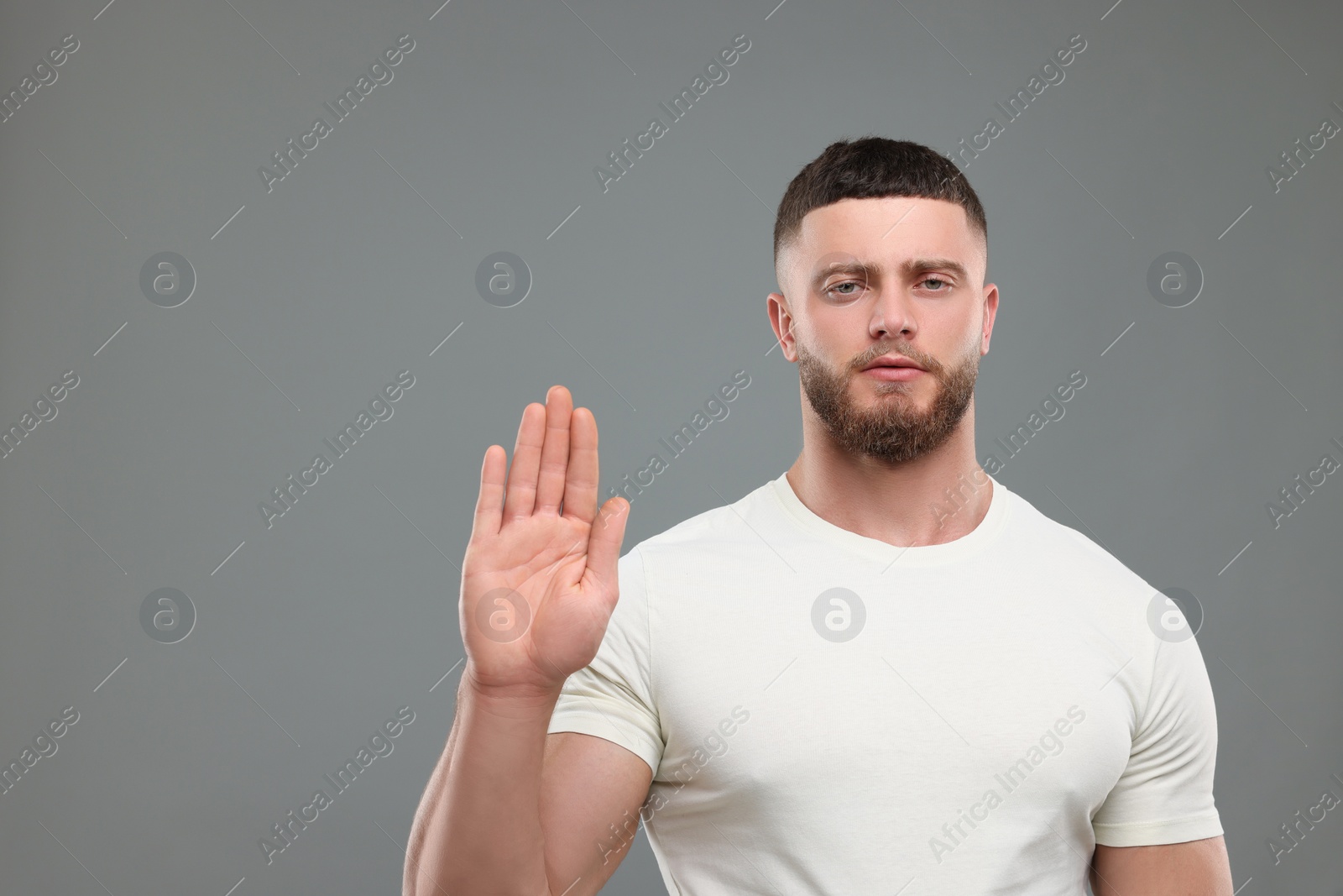 Photo of Man showing stop gesture on grey background. Space for text
