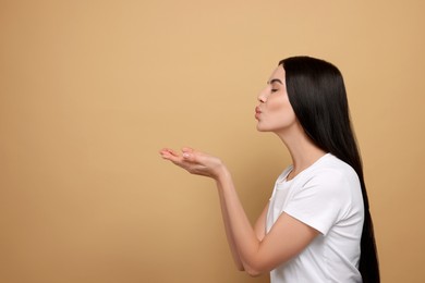 Photo of Beautiful young woman blowing kiss on beige background. Space for text