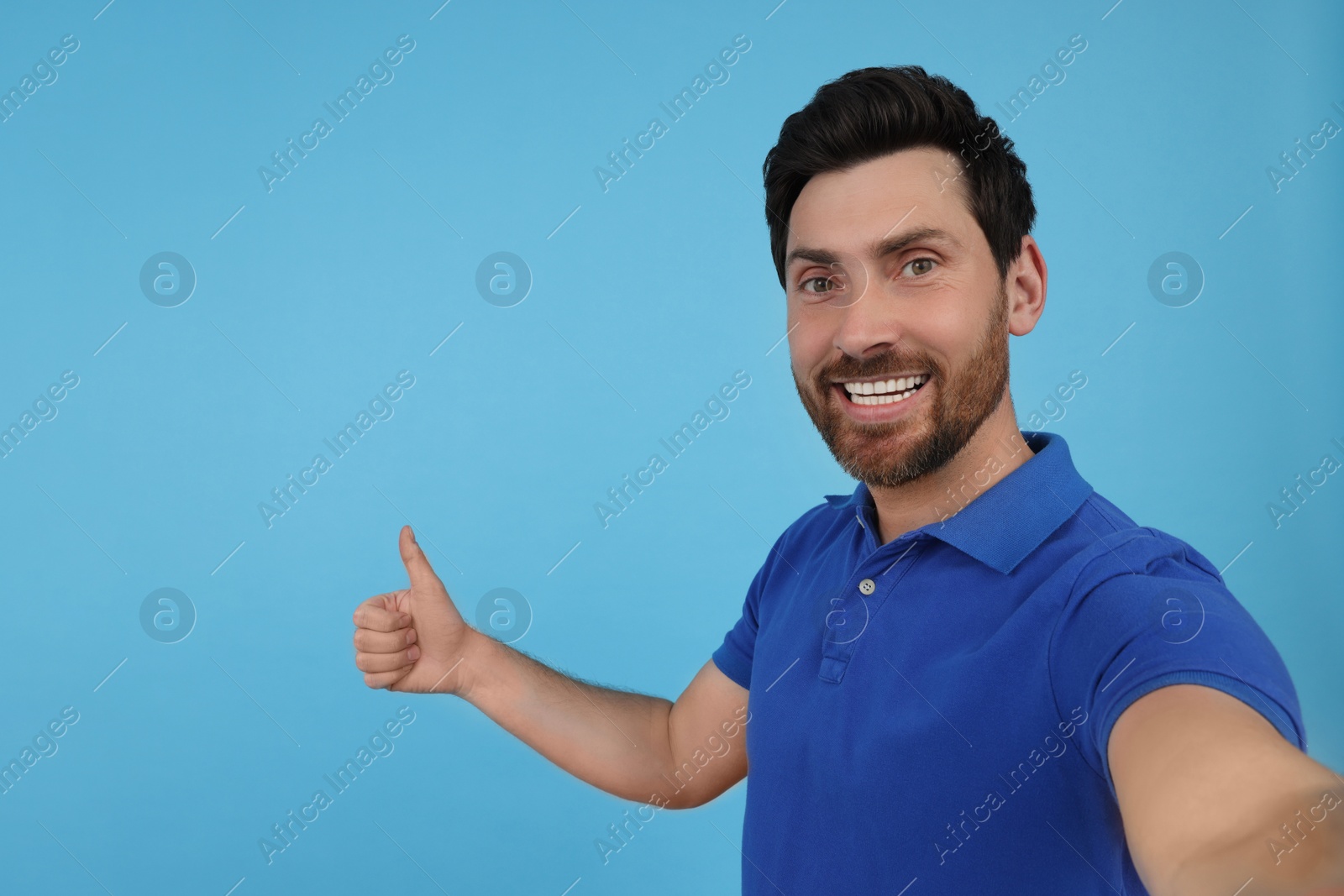 Photo of Emotional man taking selfie and showing thumbs up on light blue background, space for text
