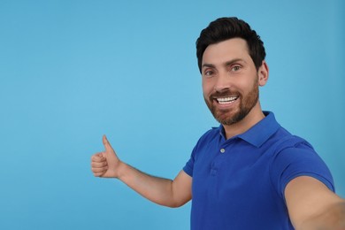 Photo of Emotional man taking selfie and showing thumbs up on light blue background, space for text