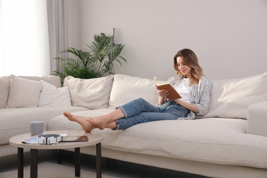 Photo of Young woman reading book on sofa at home