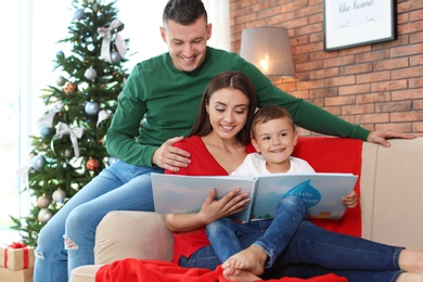 Photo of Happy parents and child reading fairy tales together at home on Christmas day