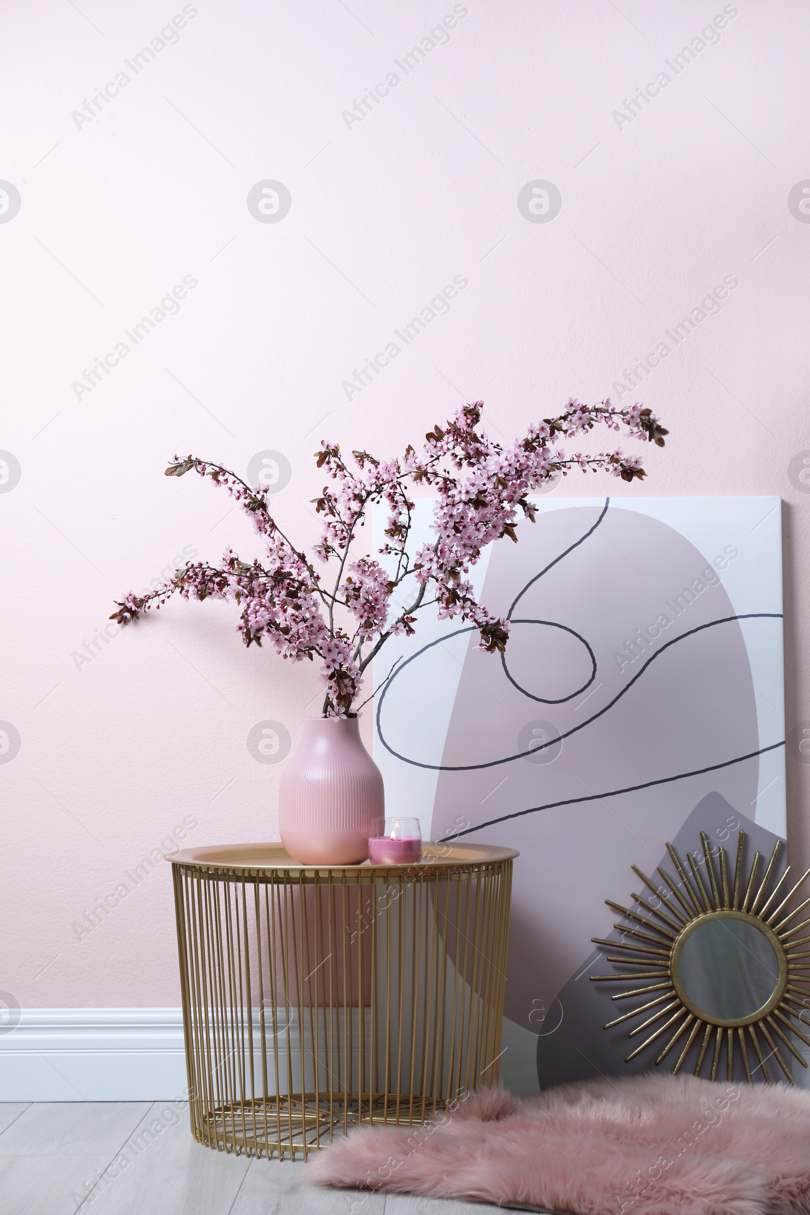 Photo of Blossoming tree twigs in vase on table near pink wall indoors