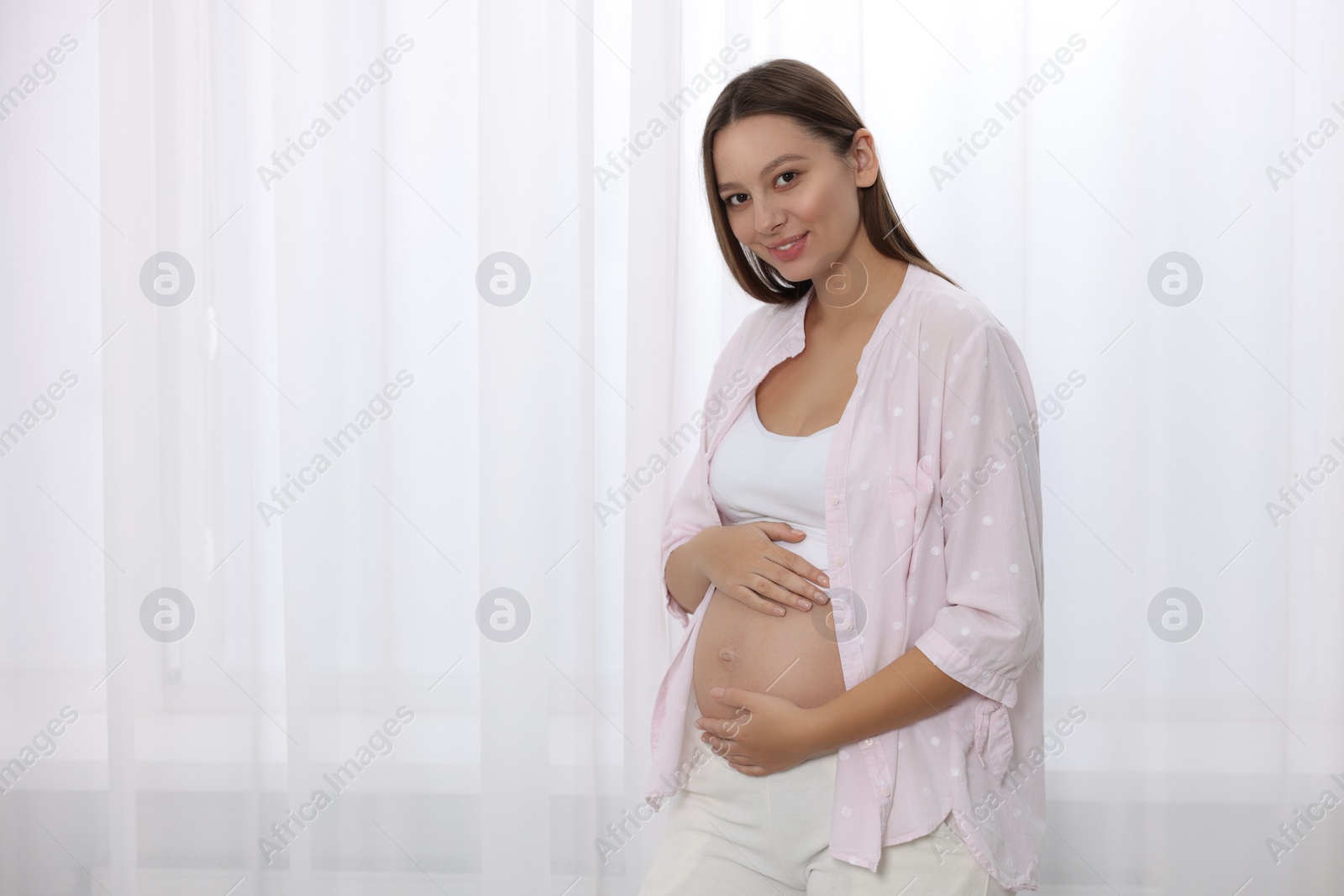 Photo of Beautiful pregnant woman near window indoors, space for text