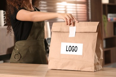 Image of Woman holding paper bag with logo at counter in cafe, closeup