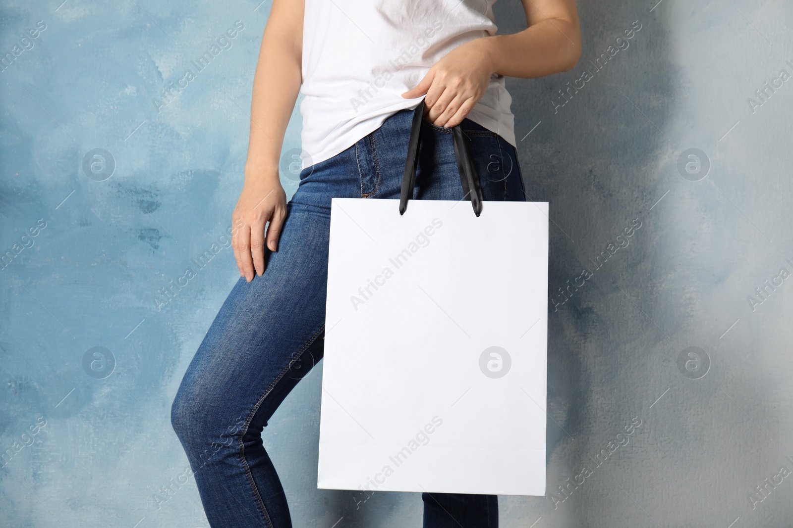 Photo of Woman holding mock-up of paper shopping bag on color background