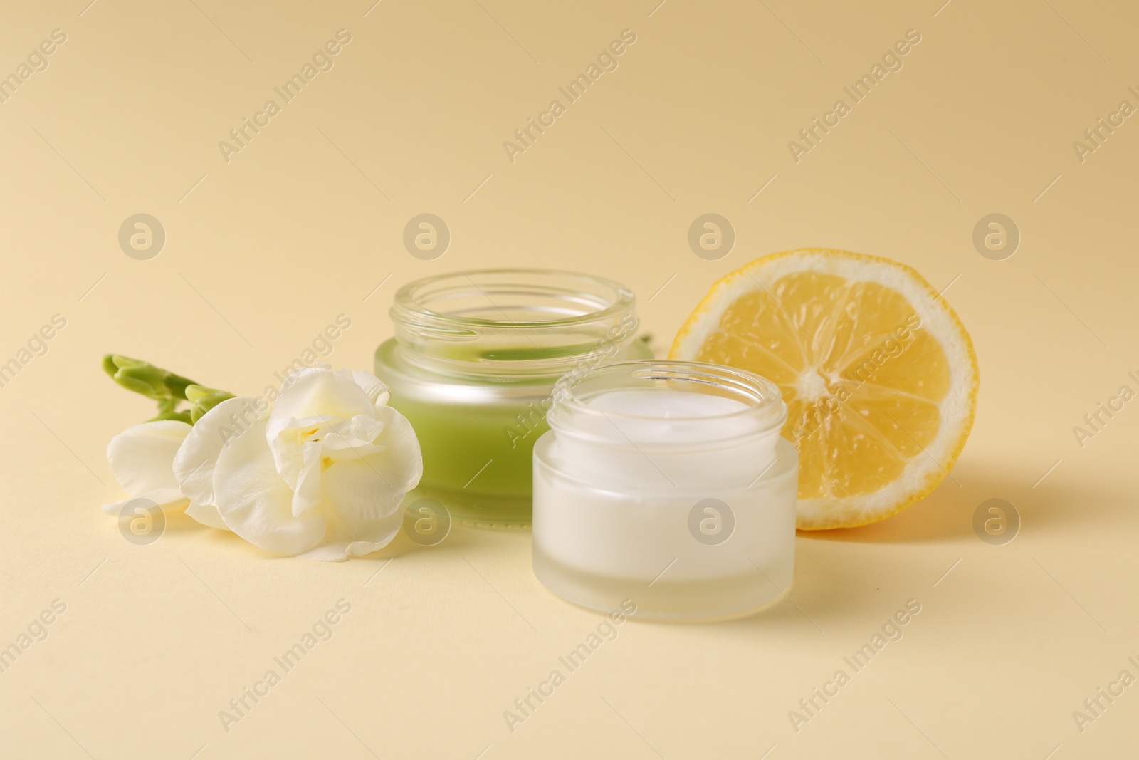 Photo of Moisturizing cream in open jars, lemon and freesia flower on beige background. Body care products