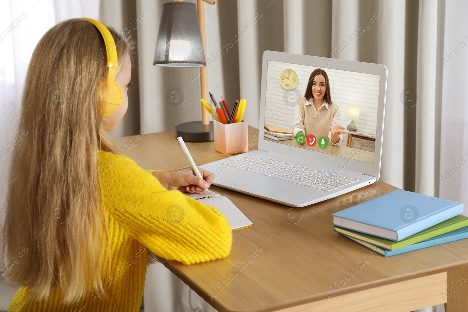 Image of E-learning. Little girl taking notes during online lesson at wooden table indoors