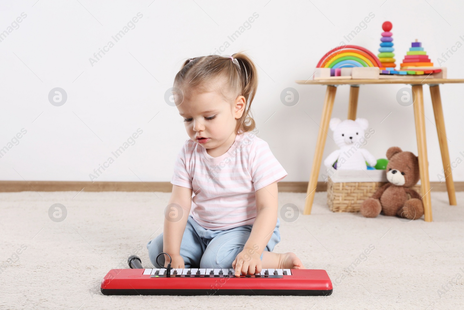 Photo of Cute little girl playing with toy piano at home