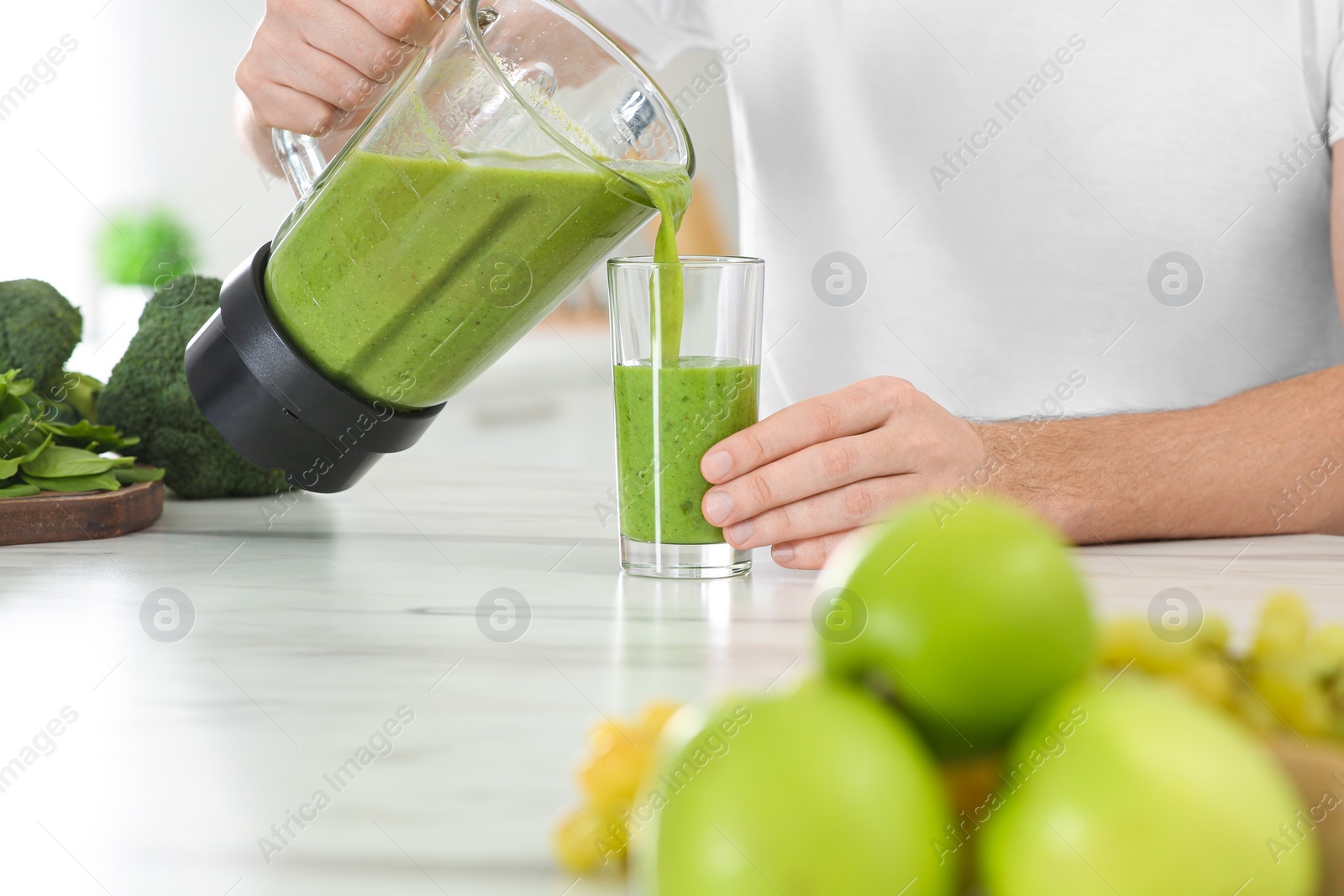 Photo of Man pouring delicious smoothie into glass at white marble table, closeup