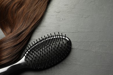 Photo of Stylish brush with brown hair strand on dark grey table, top view. Space for text