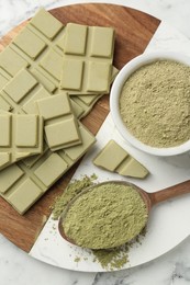 Pieces of tasty matcha chocolate bar and powder on white table, top view