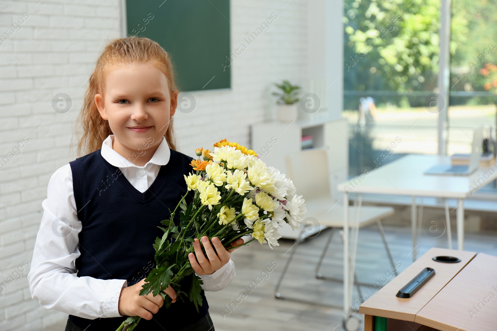 Photo of Happy schoolgirl with bouquet in classroom. Teacher's day