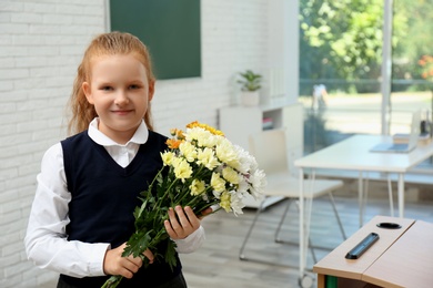 Happy schoolgirl with bouquet in classroom. Teacher's day