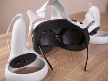 Modern virtual reality headset, glasses and controllers on wooden table, closeup