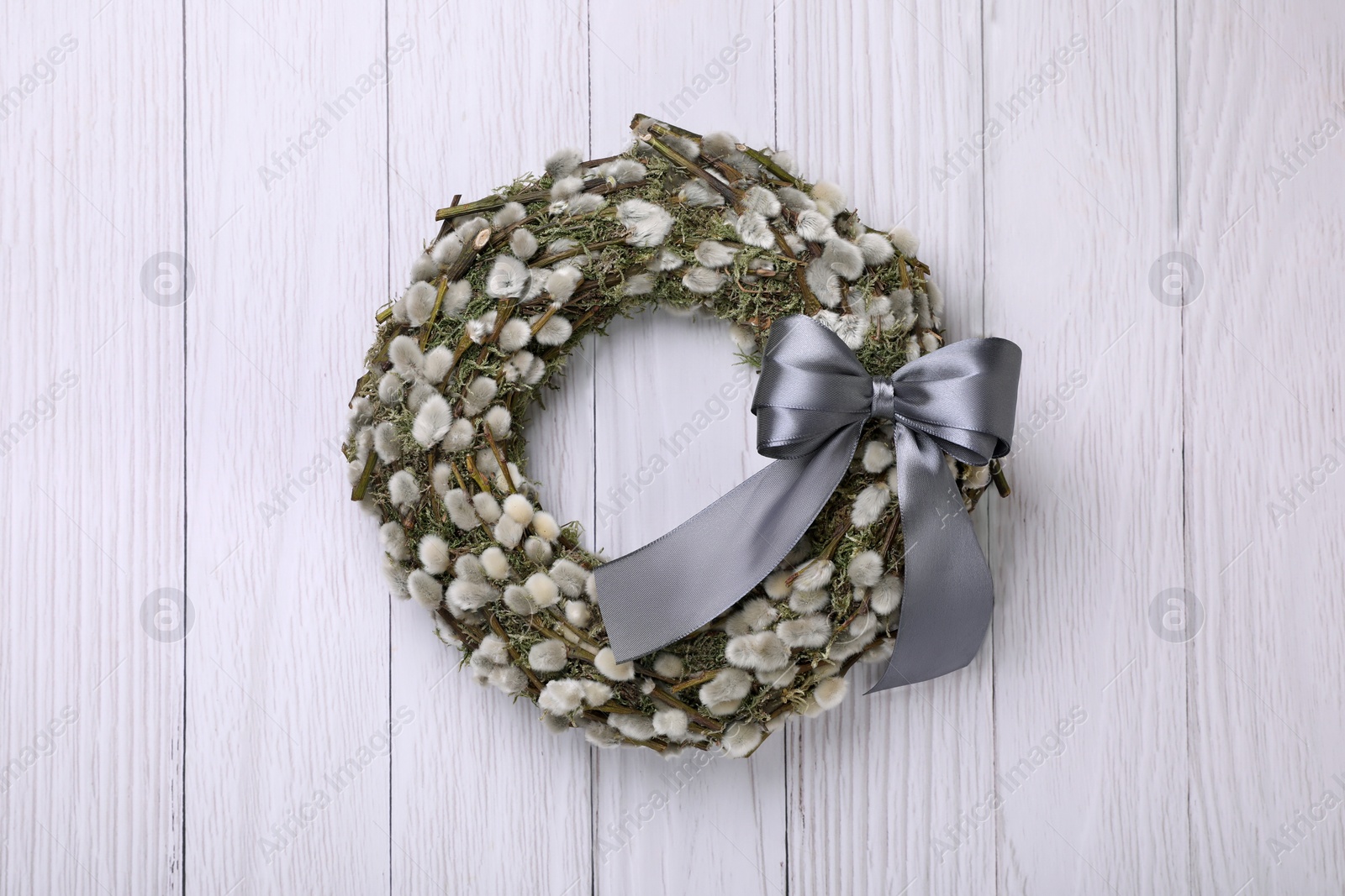 Photo of Wreath made of beautiful willow branches and grey bow on white wooden background, top view