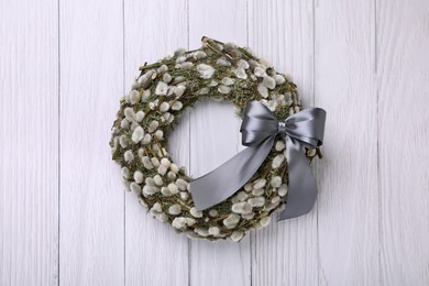 Photo of Wreath made of beautiful willow branches and grey bow on white wooden background, top view