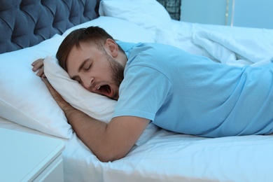 Photo of Young man yawning while sleeping in bed at night