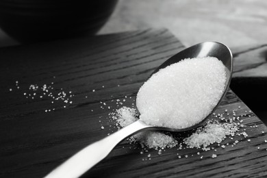 Photo of Spoon with granulated sugar on black wooden board, closeup