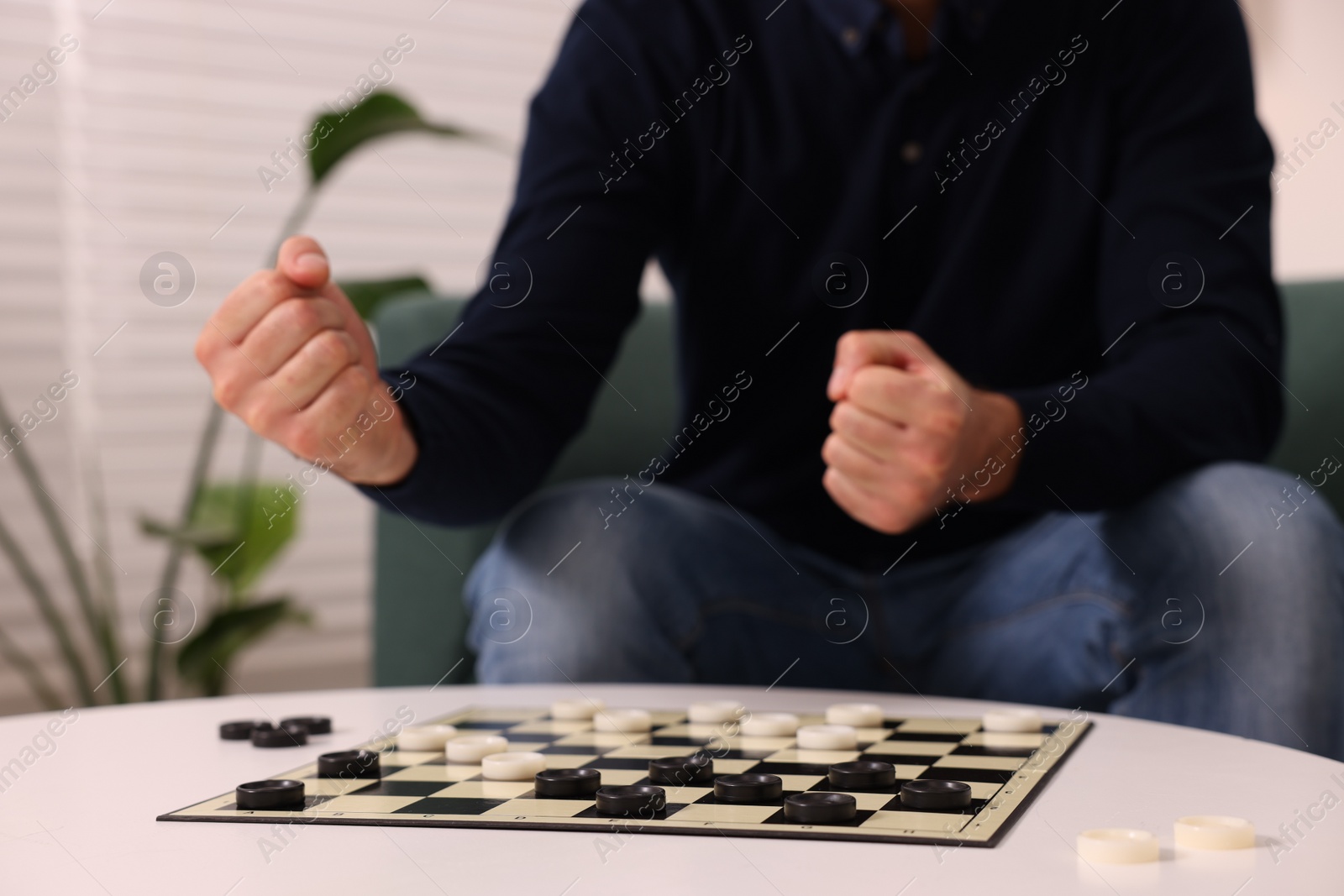 Photo of Man playing checkers at white table indoors, closeup