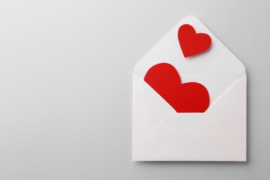 Red paper hearts and envelope on white background, top view