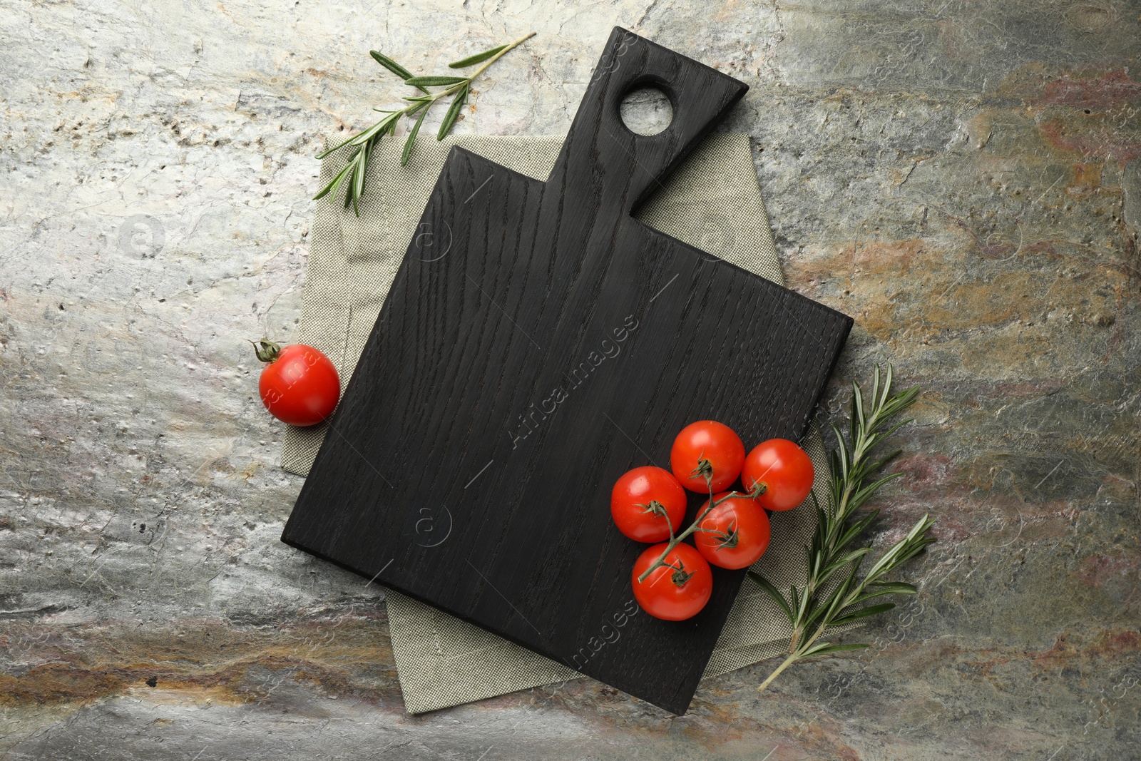 Photo of Black cutting board, tomatoes and rosemary on textured table, flat lay