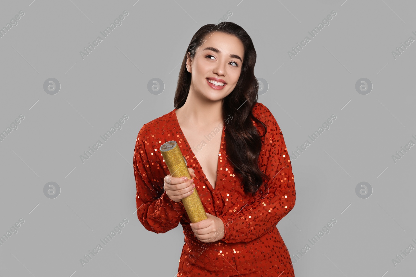 Photo of Young woman blowing up party popper on light grey background, space for text