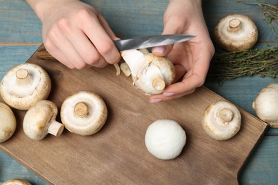 Photo of Young woman peeling fresh champignon mushrooms at table, closeup