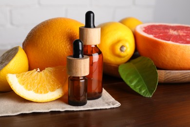 Photo of Bottles of essential oils with different citrus fruits and leaf on wooden table, closeup