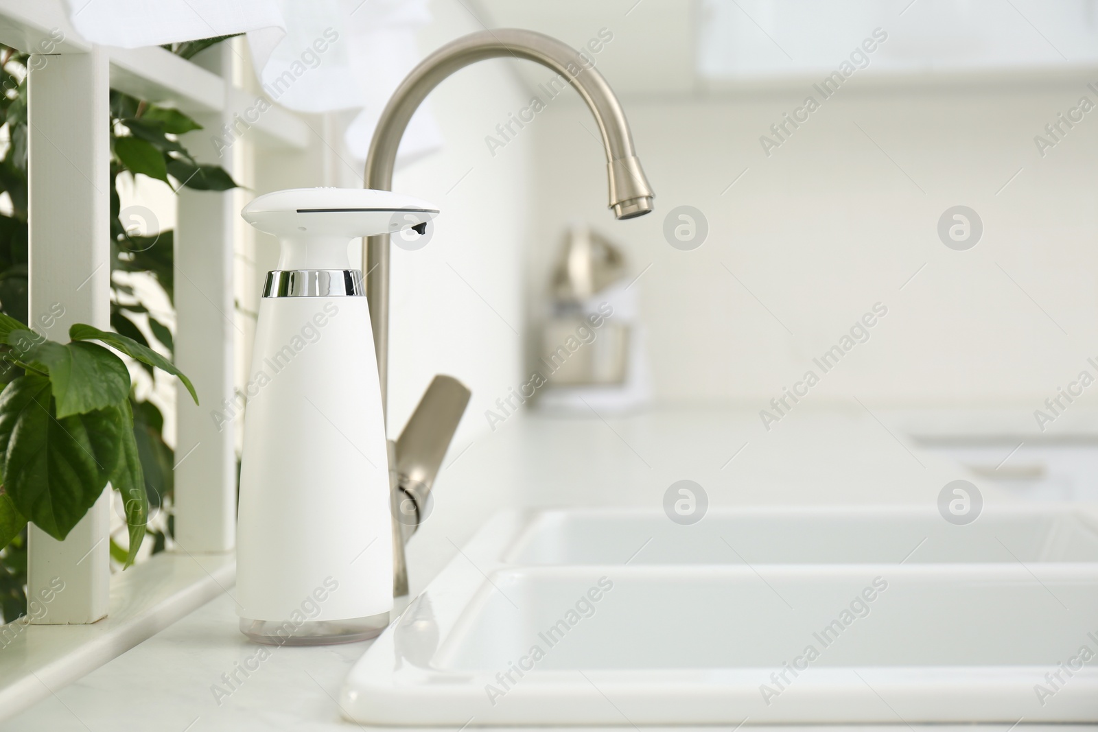 Photo of Modern automatic soap dispenser near sink in kitchen. Space for text