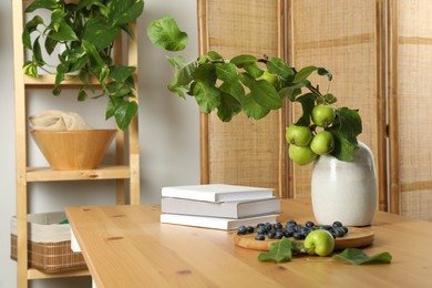 Books, blueberries and branch with green apples on wooden table in room